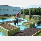 Laying rubber chippings around raised beds & alan puncturing the tarpaulin for drainage